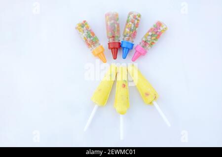 Die bunten süßen Anisbohnen Plastikflaschen mit gelber Creme Lollypop isoliert auf weißem Hintergrund. Stockfoto