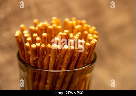 Salziges Brot Streifen in einer Glastasse und auf einem Hintergrund von groben homespun Stoff verstreut. Nahaufnahme, selektiver Fokus. Stockfoto