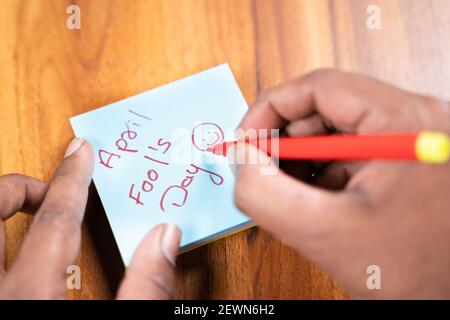 POV Schuss der Hände schreiben April Narren Tag auf Haftnotizen, Konzept der Vorbereitung für Streich oder Narren Tag Feier. Stockfoto