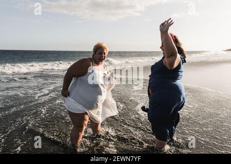 Kurvige Frauen tanzen am Strand und haben Spaß im Sommer Urlaub - Fokus auf linke Frau Stockfoto