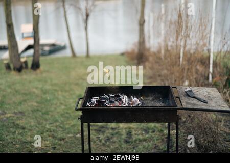 Brazier Kochen im Freien kleine Fluss Feuer Boot im Hintergrund Und Bäume Stockfoto