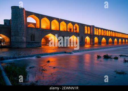 Isfahan, Iran - 14,04.2019: Einbruch der Dunkelheit an der Si O SE Pol Brücke, Isfahan, Iran. Orangefarbene Lichter auf der Brücke stehen im Kontrast zum verblassenden blauen Himmel. Stockfoto