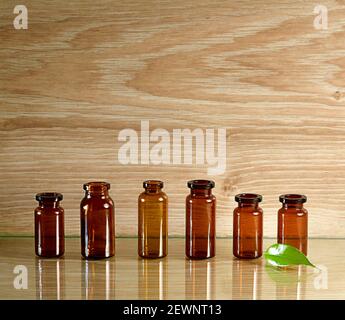 Leere Flaschen aus dunkelbraunem und bernsteinfarbenem Glas. Auf einer Glasoberfläche, auf einem warmen Holzhintergrund. Mit einem grünen frischen Blatt. Stockfoto
