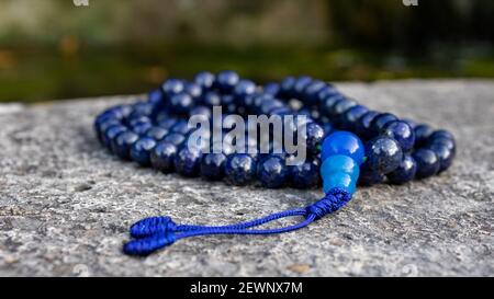 Blaue buddhistische mala Gebetsperlen (Lapislazuli) auf Stein, aus der Nähe. Achtsamkeit und japa Meditationszubehör. Stockfoto