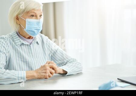 Alte Frau in medizinische Maske mit Beratung mit Arzt in Klinik Stockfoto