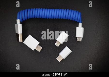 Blaues Spiral-USB-Kabel mit Adaptern für Micro, Mini-USB und Blitz isoliert auf dunklem Hintergrund Stockfoto