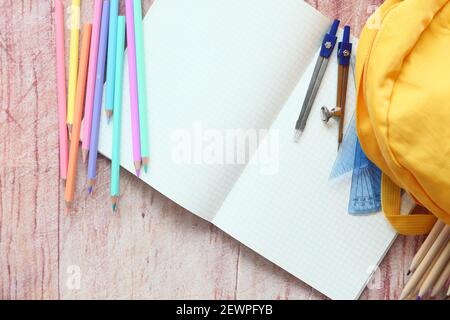 Draufsicht auf gelben Rucksack mit verschiedenen bunten Papeterie auf Tisch. Stockfoto