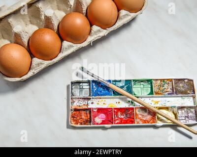 Schachteln mit Eiern und Farben mit Pinsel auf weißem Tisch. Stockfoto