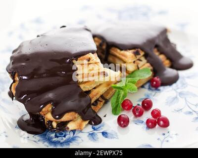 Waffeln in Form von Herzen gekrönt mit heißer Schokolade Und mit Preiselbeeren auf vintage französischen Teller mit Besteck Stockfoto