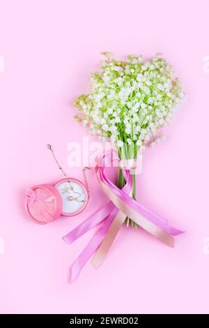 Ein Bouquet von Maiglöckchen blüht mit rosa Bänder und eine rosa Box mit einem goldenen Armband auf Ein rosa Hintergrund Nahaufnahme Stockfoto