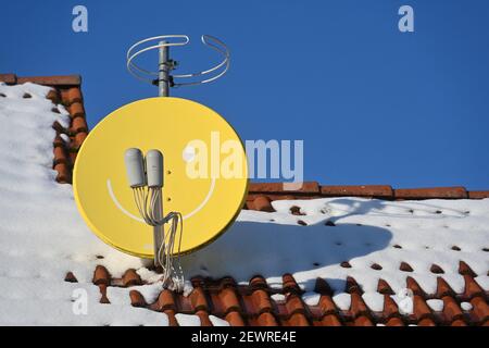 Leipziger Land, Deutschland. Februar 2021, 11th. Auf einem verschneiten Dach in Leipzig steht eine Satellitenschüssel mit Gesicht. Quelle: Volkmar Heinz/dpa-Zentralbild/ZB/dpa/Alamy Live News Stockfoto