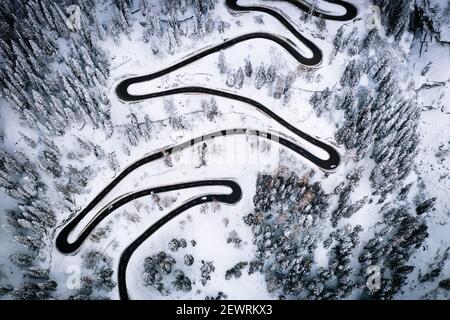 Luftaufnahme von Autos auf engen Kurven der Bergstraße durch den verschneiten Wald, Schweiz, Europa Stockfoto