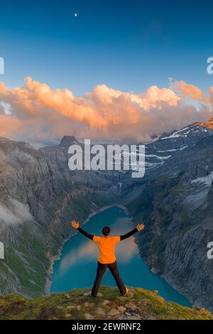 Mann mit ausgestreckten Armen, der den Sonnenuntergang über dem See Limmernsee genießt, der auf Felsen steht, Kanton Glarus, Schweiz, Europa Stockfoto
