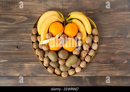 Draufsicht auf verschiedene Früchte und getrocknete Früchte bilden ein Herz auf einem dunklen Holz Hintergrund. Gesundes Essen und Wellness-Konzept. Leerzeichen für Text. Stockfoto