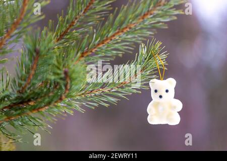 Der weiße Teddybär des Neujahrs hängt an einem Zweig eines Weihnachtsbaums im Wald. Hochwertige Fotos Stockfoto