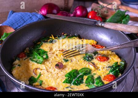 Hausgemachtes Reisomelett mit roten Zwiebeln, Spinat und Tomaten in einer Pfanne Stockfoto