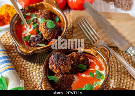 Veganes Gericht mit orientalisch würziger Tomatensuppe und Linsennüssen Fleischbällchen serviert in rustikalen braunen Schalen mit Kokosmilch gekrönt Stockfoto