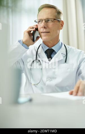 Schöner männlicher Arzt im Gespräch auf Handy in der Klinik Stockfoto