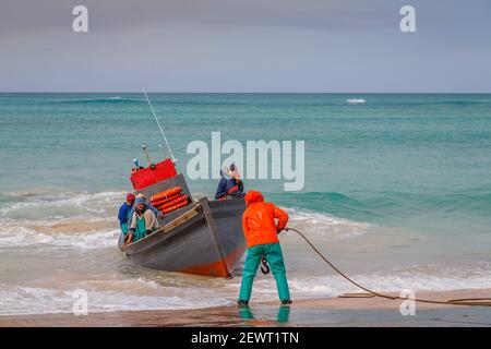 Farbenfroh gekleidete Fischer, die ihr Boot am lokalen Fischereihafen in Arniston, Provinz Western Cape, Südafrika, ausbeben Stockfoto