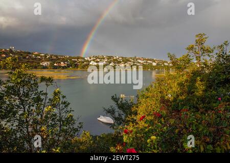 Ein Regenbogen über Bushmans Fluss mit einem Boot auf dem Fluss und Sturm Wolken in der Ferne. Eastern Cape Province, Südafrika Stockfoto