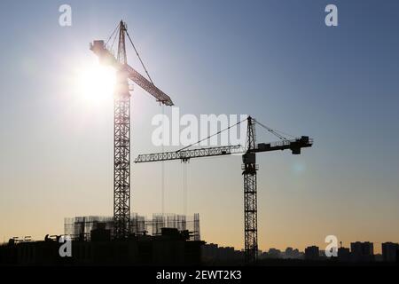 Silhouetten von Baukräne und unfertigen Wohngebäuden auf Sonnenaufgang Hintergrund. Wohnungsbau, Wohnblock in der Stadt Stockfoto