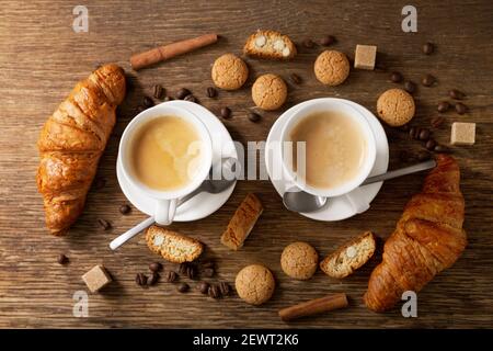 Zwei Tassen Kaffee mit Croissants auf einem Holztisch, Blick von oben Stockfoto