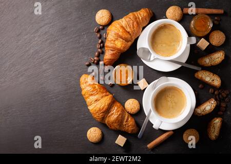 Zwei Tassen Kaffee mit Croissants auf dunklem Hintergrund, Draufsicht Stockfoto