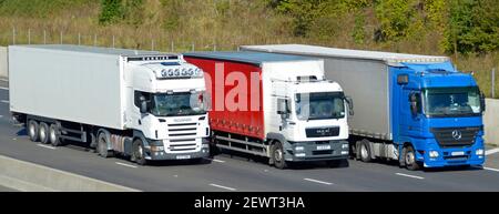 Versetzte Front- und Seitenansicht Gruppe von drei rot weiß Und blaue lkw-Lieferkettenschlepper transportieren LKW-Überholmanschette Vierspurige Autobahn England Großbritannien Stockfoto