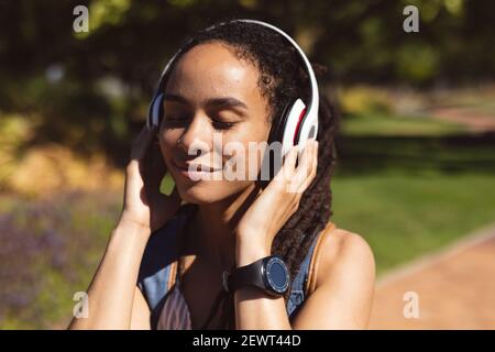 Lächelnde afroamerikanische Frau trägt Kopfhörer auf Roller stehen hören Zur Musik auf der Straße Stockfoto