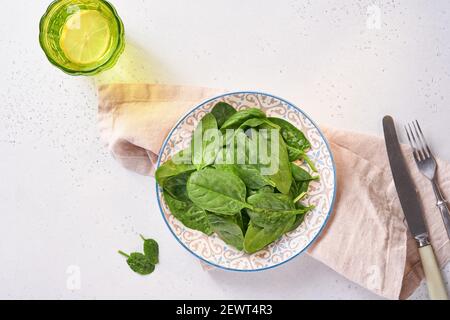 Frisches Baby Spinat Blätter in Keramik schöne Schüssel auf hellgrauem Beton Hintergrund. Modell. Draufsicht. Stockfoto