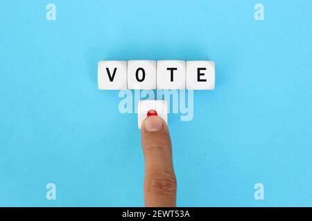 Das Wort Vote auf Holzwürfeln geschrieben mit einer männlichen Hand drücken Sie den Wahlknopf. Online-Wahlkonzept in Politik oder Business-Meetings. Stockfoto