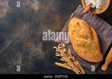 Hausgemachtes Brot mit Samen auf einem Holzständer, Weizenmehl und Ohren auf braunem alten Beton-Hintergrundtisch. Draufsicht flach liegend mit Kopierplatz Stockfoto