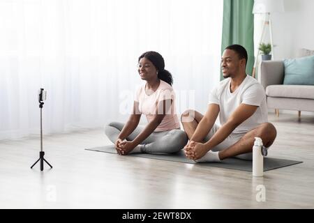 Gesundes schwarzes Paar Training auf Yoga-Matte, mit Smartphone Stockfoto