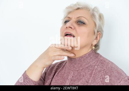 Ältere Frau mit breiten Augen und kurzen Haaren hält ihre Hände in der Nähe des Rachens, Halsschmerzen Gesundheitsprobleme Grippe Stockfoto