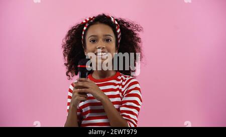 Fröhliche afroamerikanische Mädchen hält Mikrofon isoliert auf rosa Stockfoto