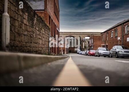 Keine Parkbeschränkungen Gelbe Linie auf der Straße niedrigen Winkel zeigt Autos geparkt geschäftigen Stadt Straße Szene. Eisenbahn Bögen Brücke Geschäfte und Häuser dramatischen Himmel Stockfoto