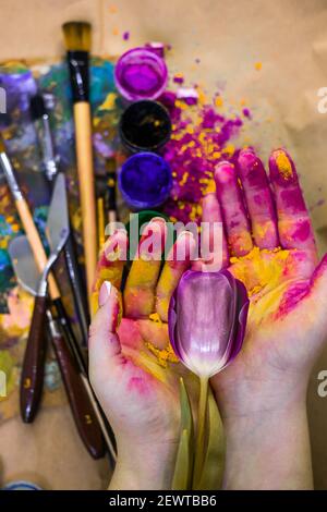 Tulpenblume in der Aquarellhand des Malers. Die Farbwerkzeuge stehen auf dem Tisch, die Gläser mit Farben und Puder sind in der Werkstatt. Stockfoto