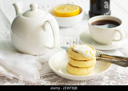 Hüttenkäse-Pfannkuchen mit saurer Sahne und Zitronenschale, serviert mit Tee. Stockfoto