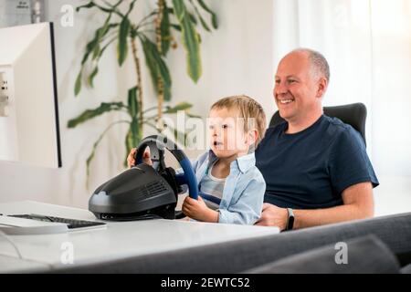 Vater und Sohn mit Spaß spielen Rennwagen Spiele auf Computer mit Lenkrad Stockfoto