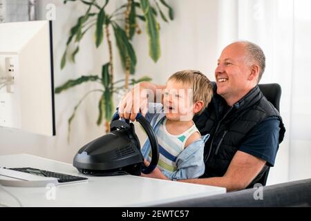 Vater und Sohn mit Spaß spielen Rennwagen Spiele auf Computer mit Lenkrad Stockfoto