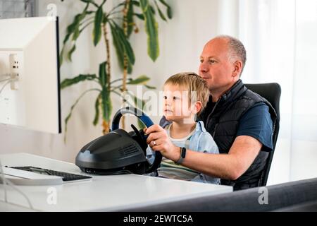 Vater und Sohn mit Spaß spielen Rennwagen Spiele auf Computer mit Lenkrad Stockfoto