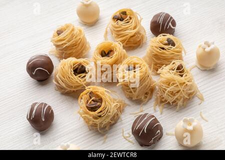 Detail der Textur der arabischen Desserts, Nest mit Nüssen, schwarzen und weißen Schokoladenkugeln, Studio mit Holzhintergrund Stockfoto