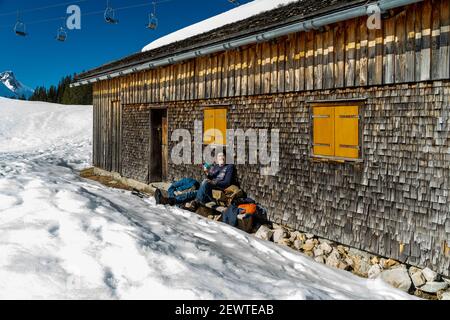 Pause auf der Bank an einer geschindelten Alphütte. Pause auf der Bank bei einer Schindelhütte. Wintersport in Österreichs verschneiten alpen. Schneeschuh Stockfoto
