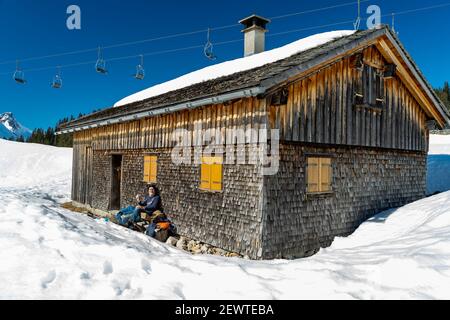 Pause auf der Bank an einer geschindelten Alphütte. Pause auf der Bank bei einer Schindelhütte. Wintersport in Österreichs verschneiten alpen. Schneeschuh Stockfoto