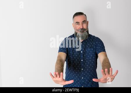 40-45-jähriger kaukasischer Hipster mit einem großen grauen Bart, mit einem ernsten Gesicht und Händen nach vorne in einem klaren Zeichen der Anordnung, ihn zu stoppen. Stockfoto