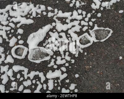 Wunderschön schmelzender Schnee um Fußabdrücke auf dem Asphalt. Stockfoto