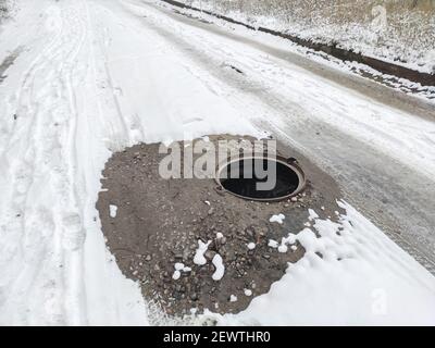 Gefährlich offene Luke auf der Straße ohne Warnung Zäune. Gefahr auf der Straße. Verschneite Straße mit offener Luke Stockfoto