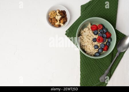 Haferflocken mit frischen Beerenfrüchten. Haferbrei in einer Schüssel mit Löffel und Heidelbeeren und Himbeeren Stockfoto