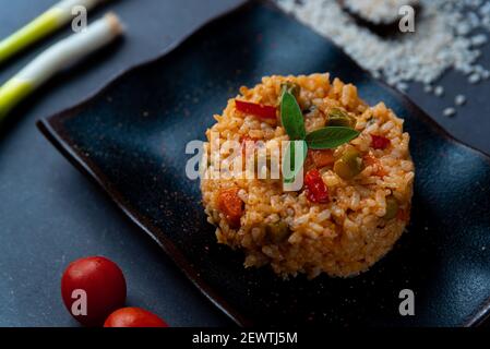 Nahaufnahme von italienischem veganem Frühlingsrisotto auf schwarzem Gericht mit rotem Pfeffer mit Salbeiblättern auf dunklem Hintergrund. Gesundes und frisches Frühlingsgemüse li Stockfoto