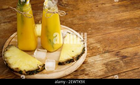 Frisch zubereitetes Ananassaft mit Eis in einem kleinen Glas Flasche auf Holzhintergrund Stockfoto